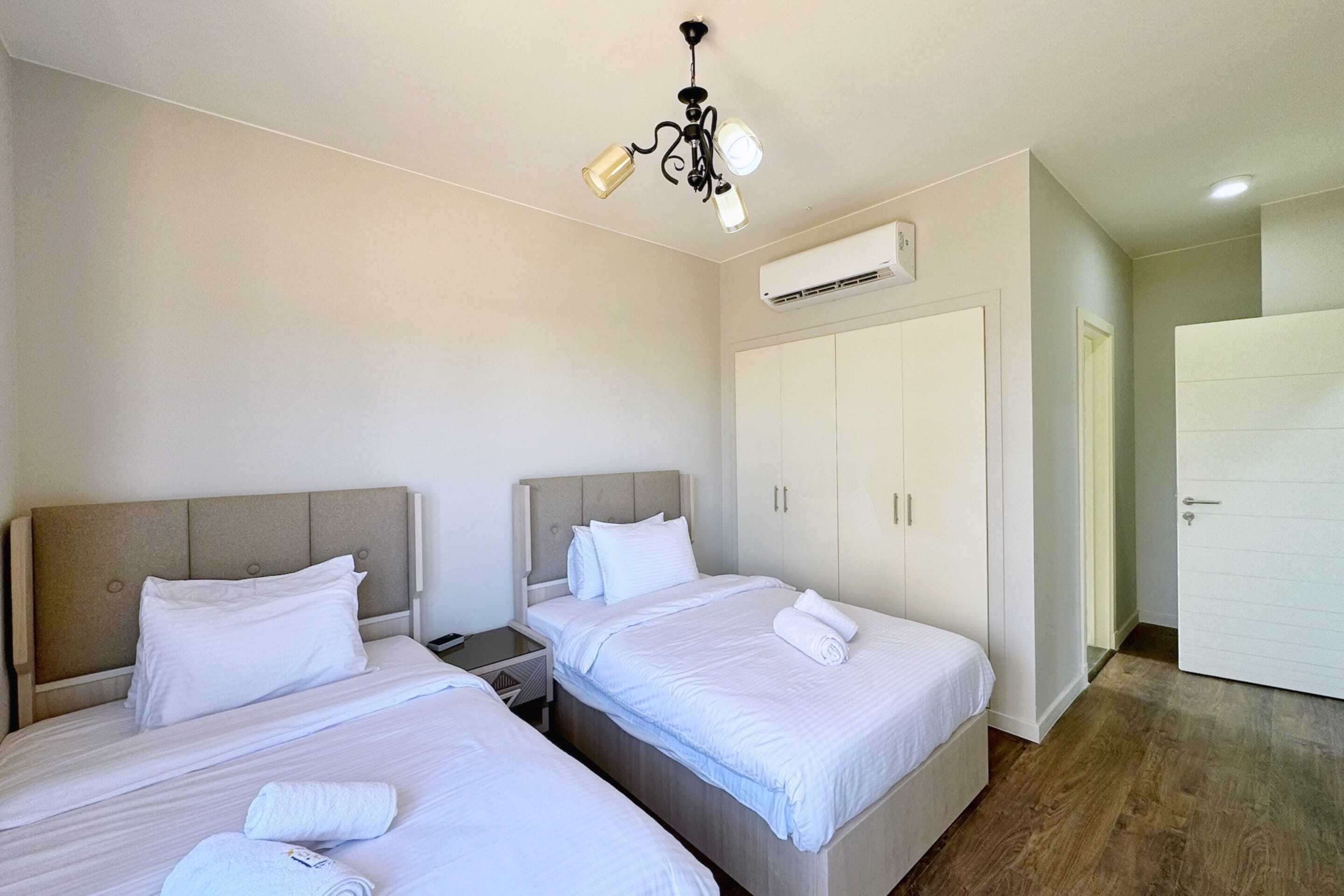 A hotel room with two single beds, a ceiling fan, an air conditioning unit, and a wardrobe.