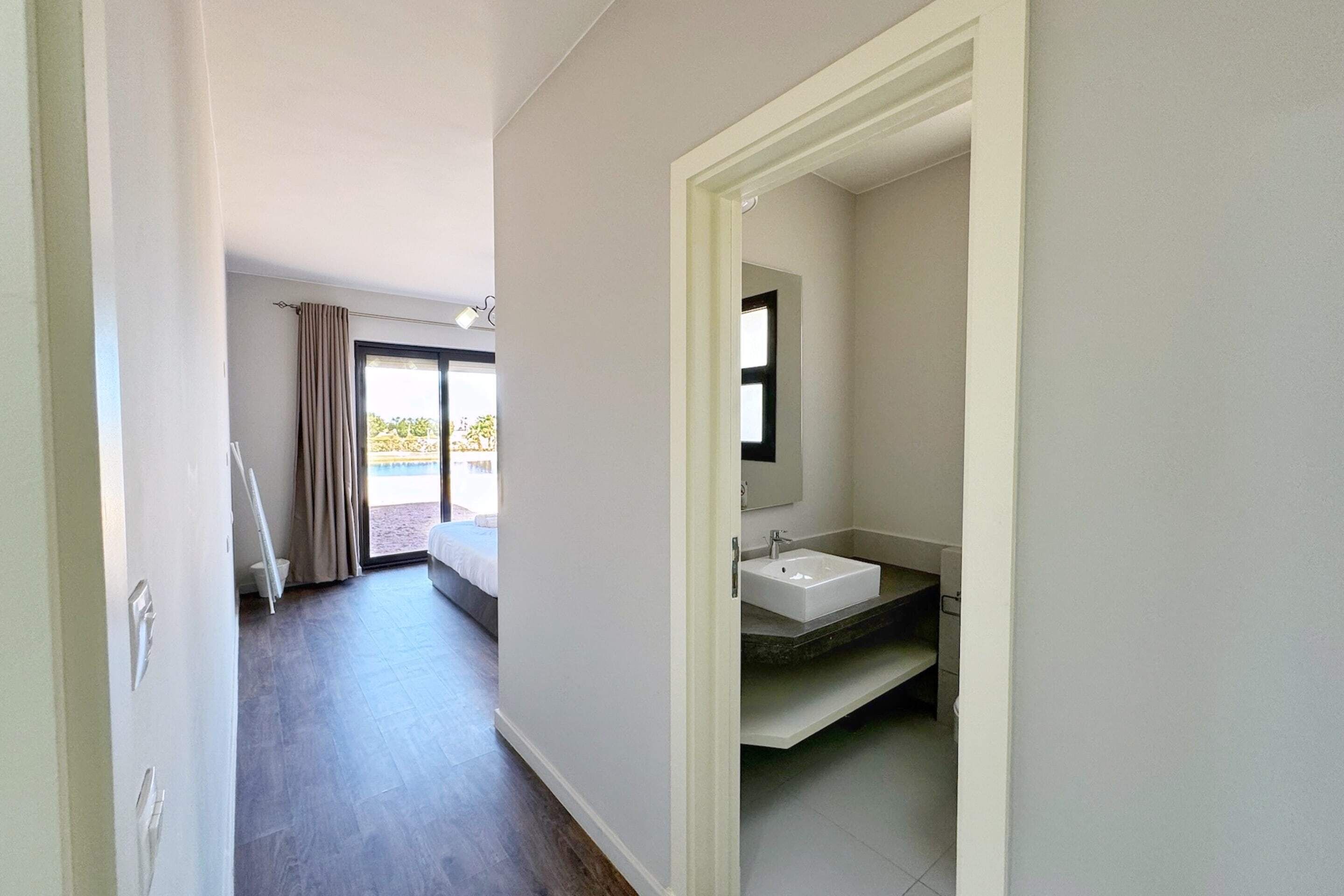 Une chambre d’hôtel avec un grand lit, une salle de bain avec un lavabo et un miroir, et une vue sur l’extérieur grâce à une porte coulissante.