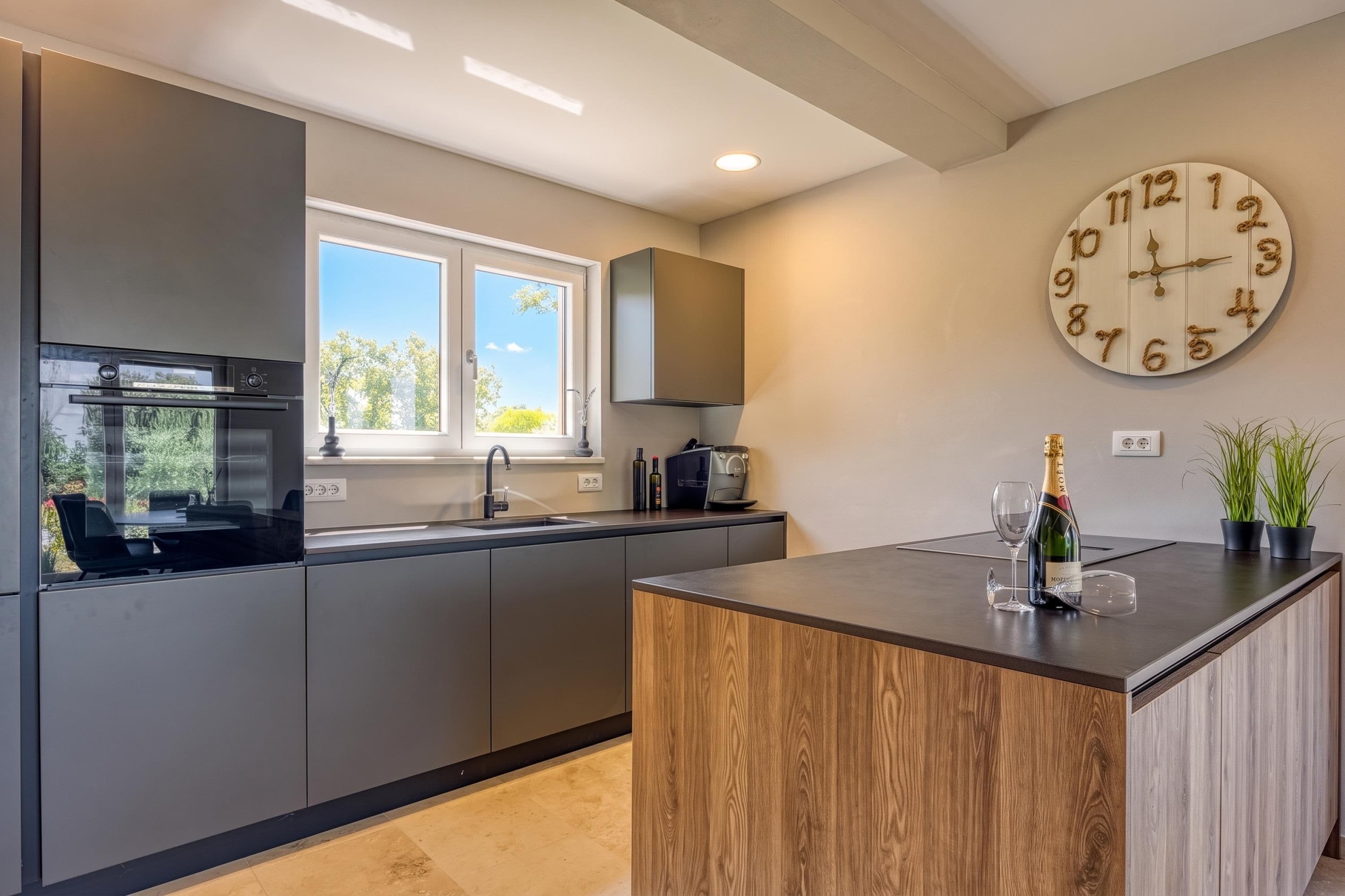 Una cocina moderna con una isla central, horno empotrado y un reloj de pared grande.