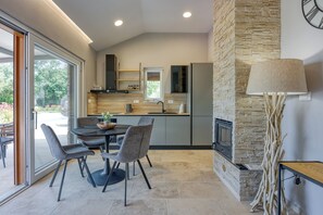 A modern kitchen with a stone fireplace, a dining area with chairs, and a large window. - Villa Tanja Lim Bay (Vrsar)
