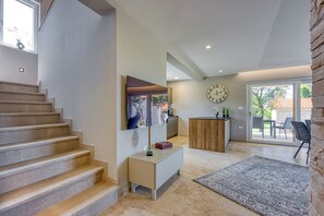 A modern interior with a staircase, a flat-screen TV, a wooden cabinet, and a large clock on the wall.
