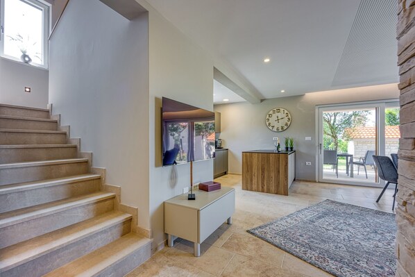 A modern interior with a staircase, a flat-screen TV, a wooden cabinet, and a large clock on the wall.