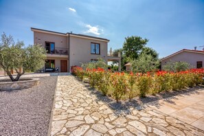A two-story building with a stone pathway leading to the entrance, surrounded by a garden with red flowers.
