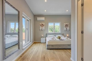 A hotel room with a large mirror, a bed with white linens, a nightstand, and two windows with artwork.