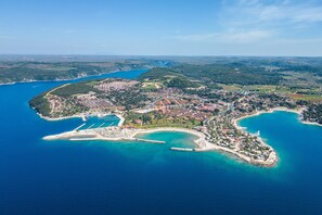 Ett flygbildsbild av en kuststad med en småbåtshamn, bostadsområden och omgivande kullar.