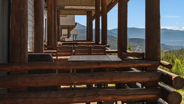 A rustic wooden deck with tables and benches, overlooking a mountainous landscape.