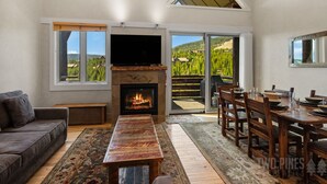A living room with a fireplace, a TV, a sofa, a dining table, and a view of a mountainous landscape.
