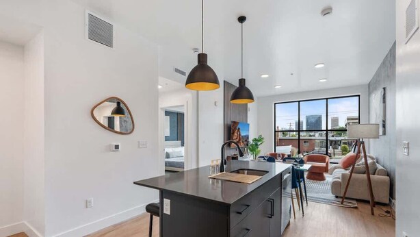 A modern kitchen with a central island, pendant lighting, and a view of the city through large windows.