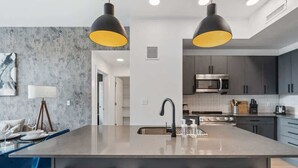 A modern kitchen with a central island, black bar stools, and pendant lighting.