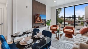 A modern dining area with a glass table, blue chairs, and a city view through large windows.