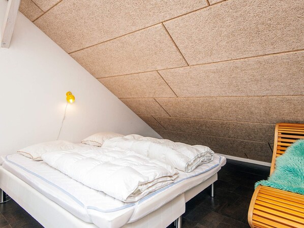 A bedroom with a bed, a wooden chair, and a wall-mounted light fixture.