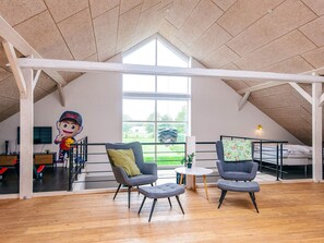 A spacious loft bedroom with a high ceiling, large windows, and a view of a green landscape.