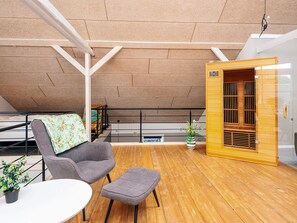 A modern loft bedroom with a wooden floor, a gray sofa, a small table, and a wooden cabinet. - 4 Star Holiday Home in Henne (Henne)