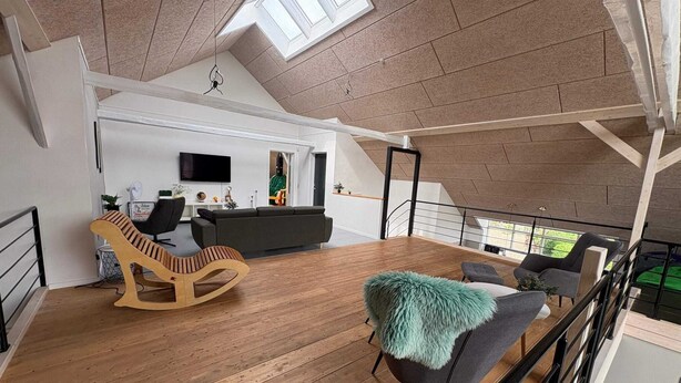 A spacious loft with a high ceiling, wooden flooring, a grey sofa, a wooden rocking chair, and a view of the outdoors through a skylight. - 4 Star Holiday Home in Henne (Henne)