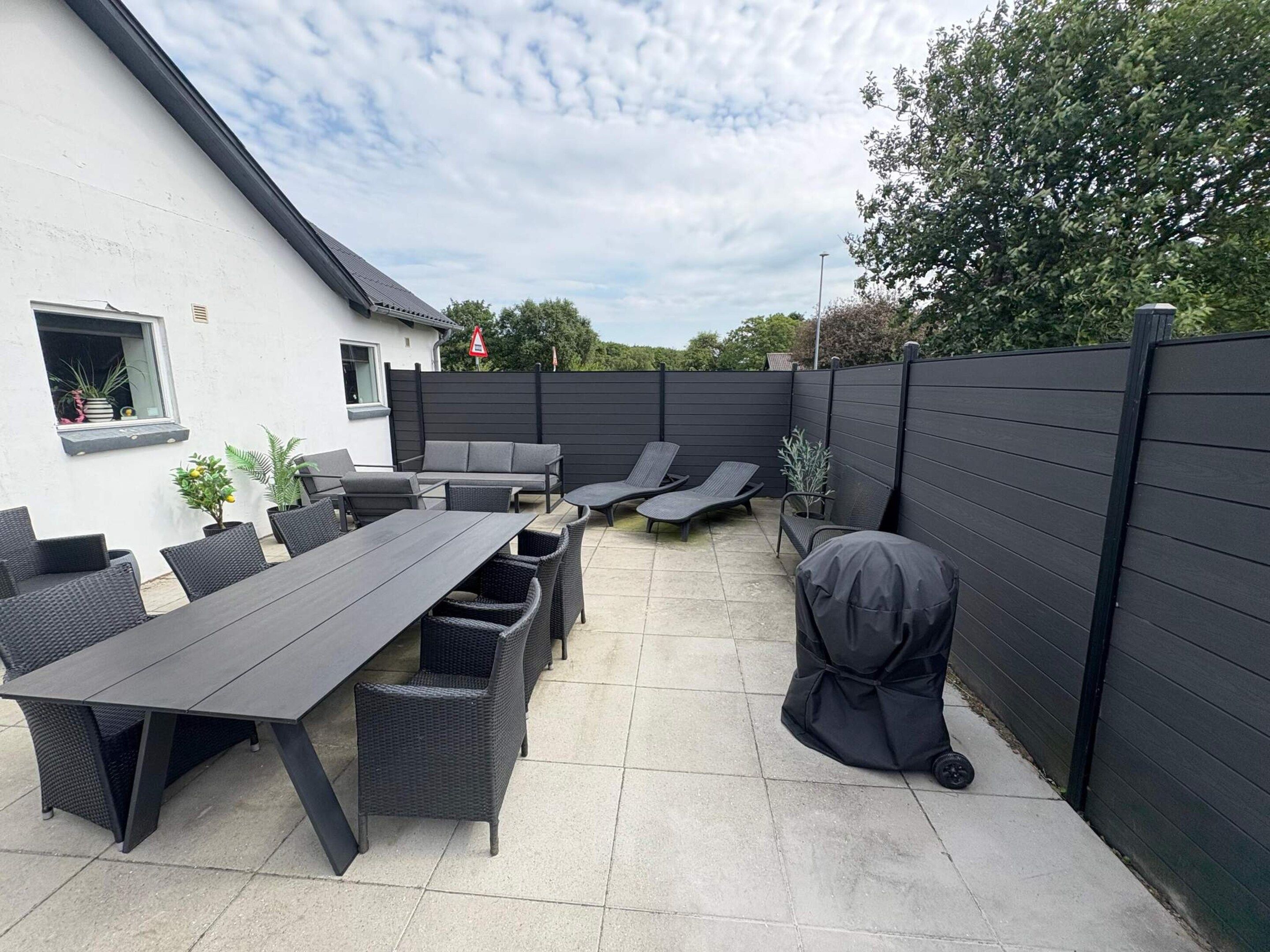 An outdoor patio area with a dining table, chairs, and a barbecue grill.