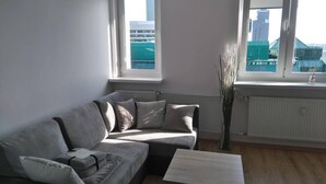 A modern living room with a grey sofa, a coffee table, and a view of a cityscape through large windows. - CityCenter ŚLISKA studio (Warszawa)