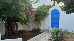 Une cour avec un bâtiment blanc, une porte bleue et des plantes en pot.