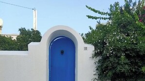 Un bâtiment blanc avec une porte bleue et une petite fenêtre au-dessus. On peut voir le numéro « 32 » sur le mur, à droite de la porte.