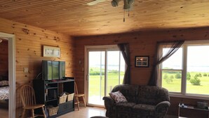 A cozy room with wooden walls and ceiling, a television, a sofa, and a view of the outdoors. - Darnley, PEI Cottage : Plan a September Getaway Today! (Kensington)
