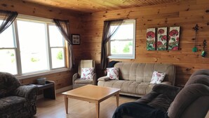A cozy cabin-style room with a sofa, armchair, and a small table. - Darnley, PEI Cottage : Plan a September Getaway Today! (Kensington)