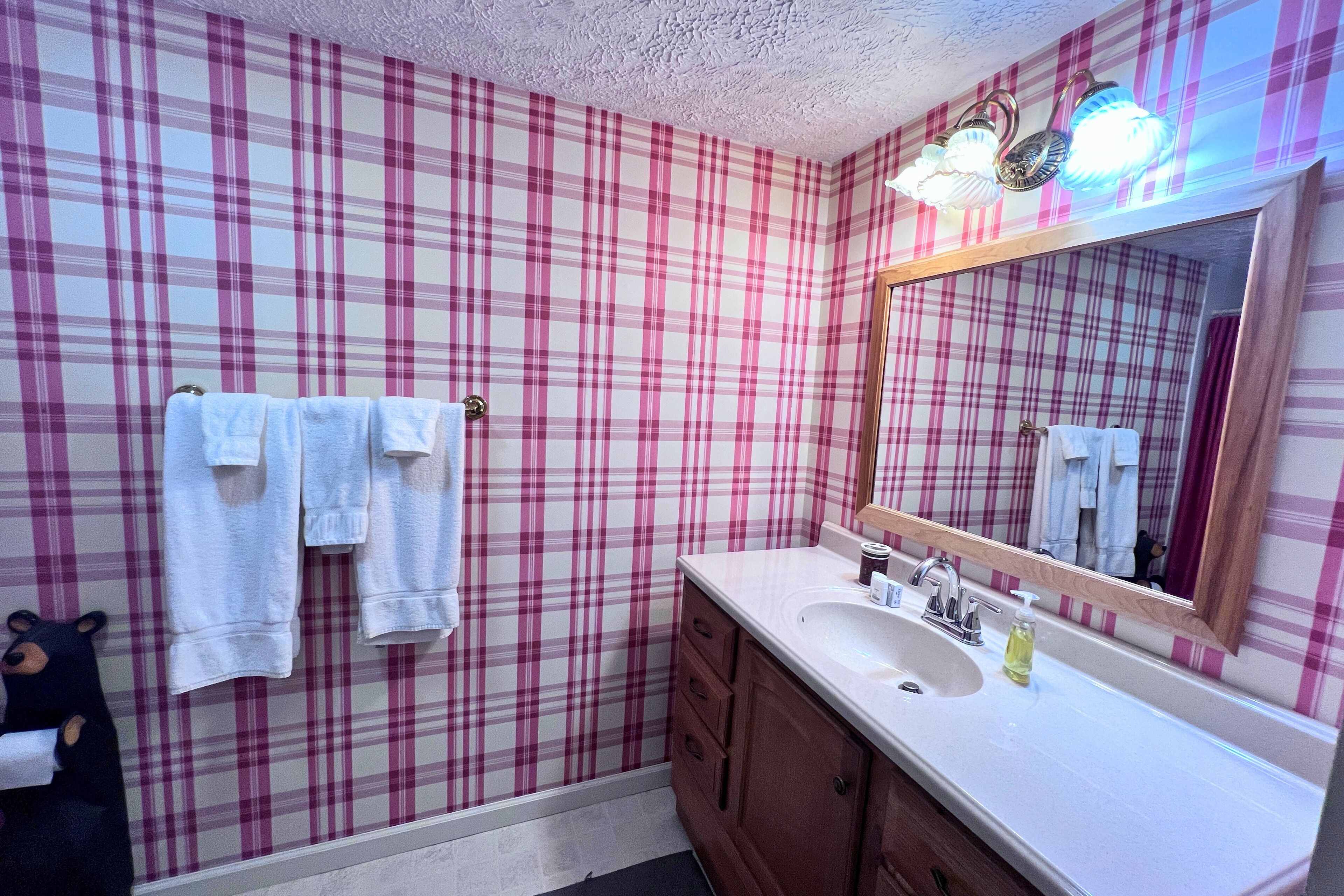 Un bagno con carta da parati a quadri, un lavandino con specchio e asciugamani appesi al muro.