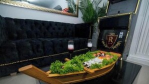 A black upholstered sofa with a glass of red wine and a wooden boat filled with green plants. - Boss-Level Hideout! (edificio calamary)