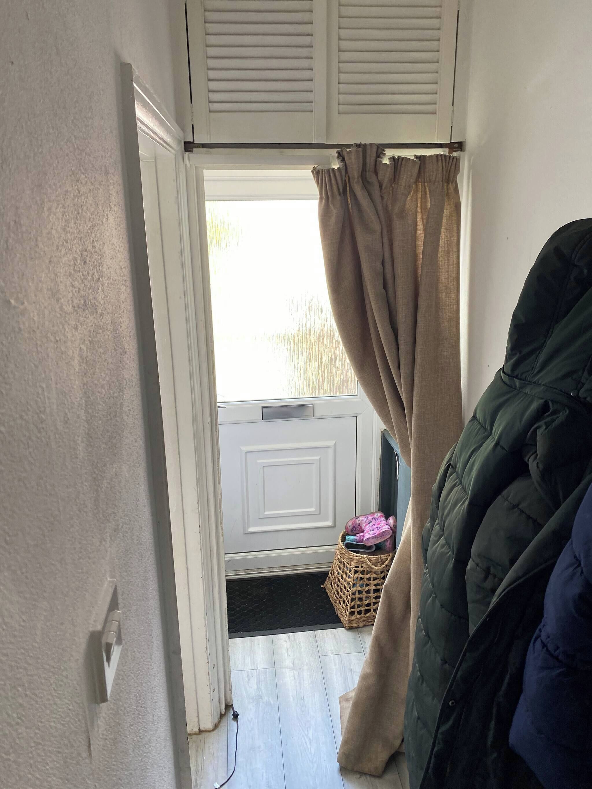 Ein Zimmer mit Fenster, Tür, Korb und einer grünen Jacke.