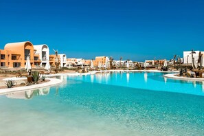 A resort with a large pool, palm trees, and modern buildings. - Xuru Stays I Prim & Pleasing 1bdr @ Kamaran El Gouna (El Gouna)