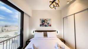 Une chambre d’hôtel moderne avec un grand lit, un tableau au mur et un balcon avec vue.