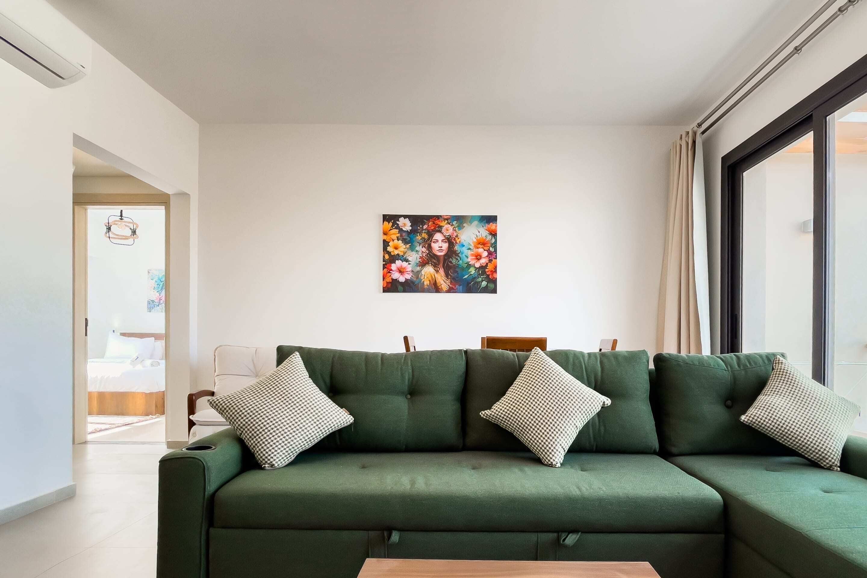 Een moderne woonkamer met een groene bank, gekleurde kussens en een schilderij aan de muur.