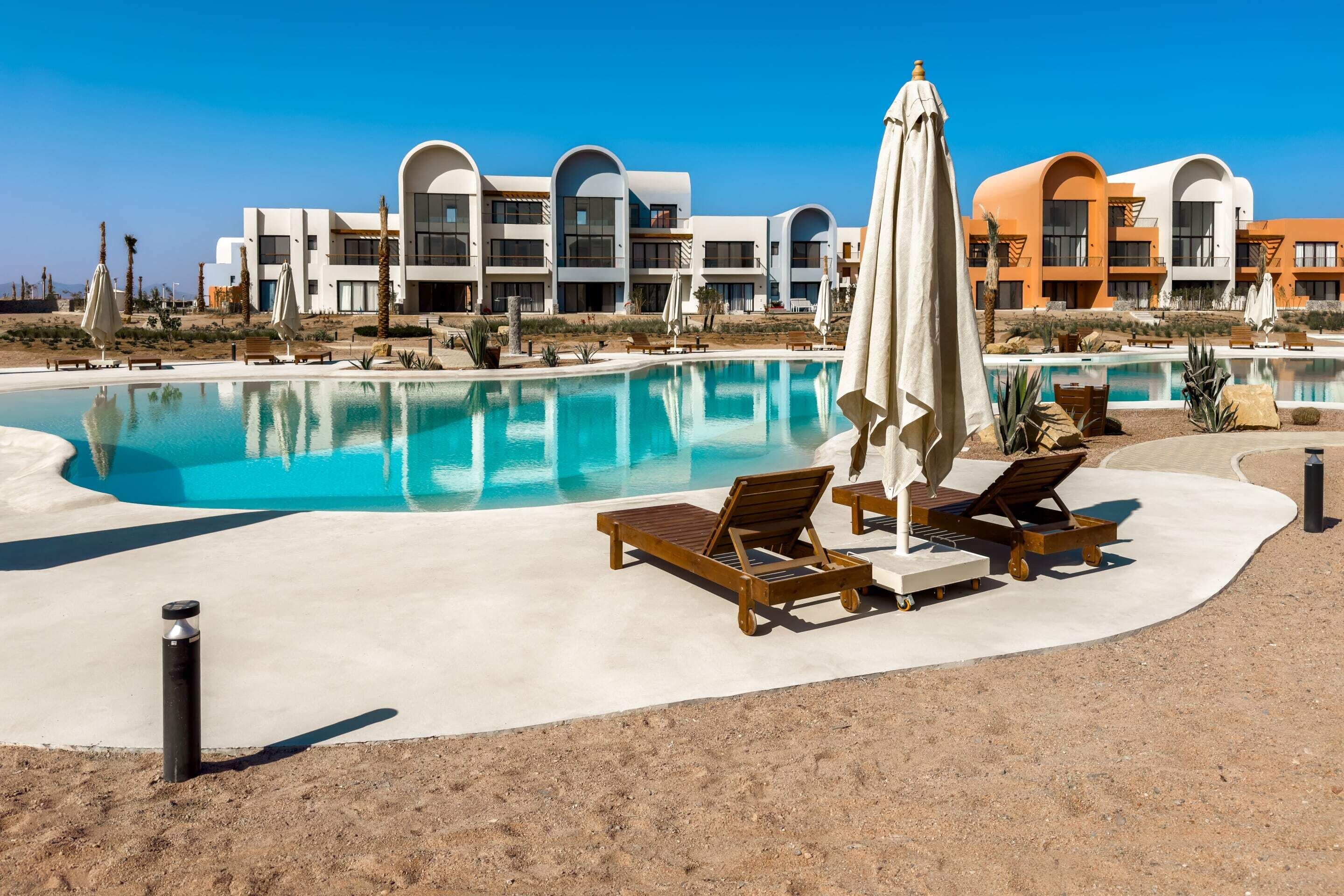 A modern hotel with a pool, sun loungers, and umbrellas.