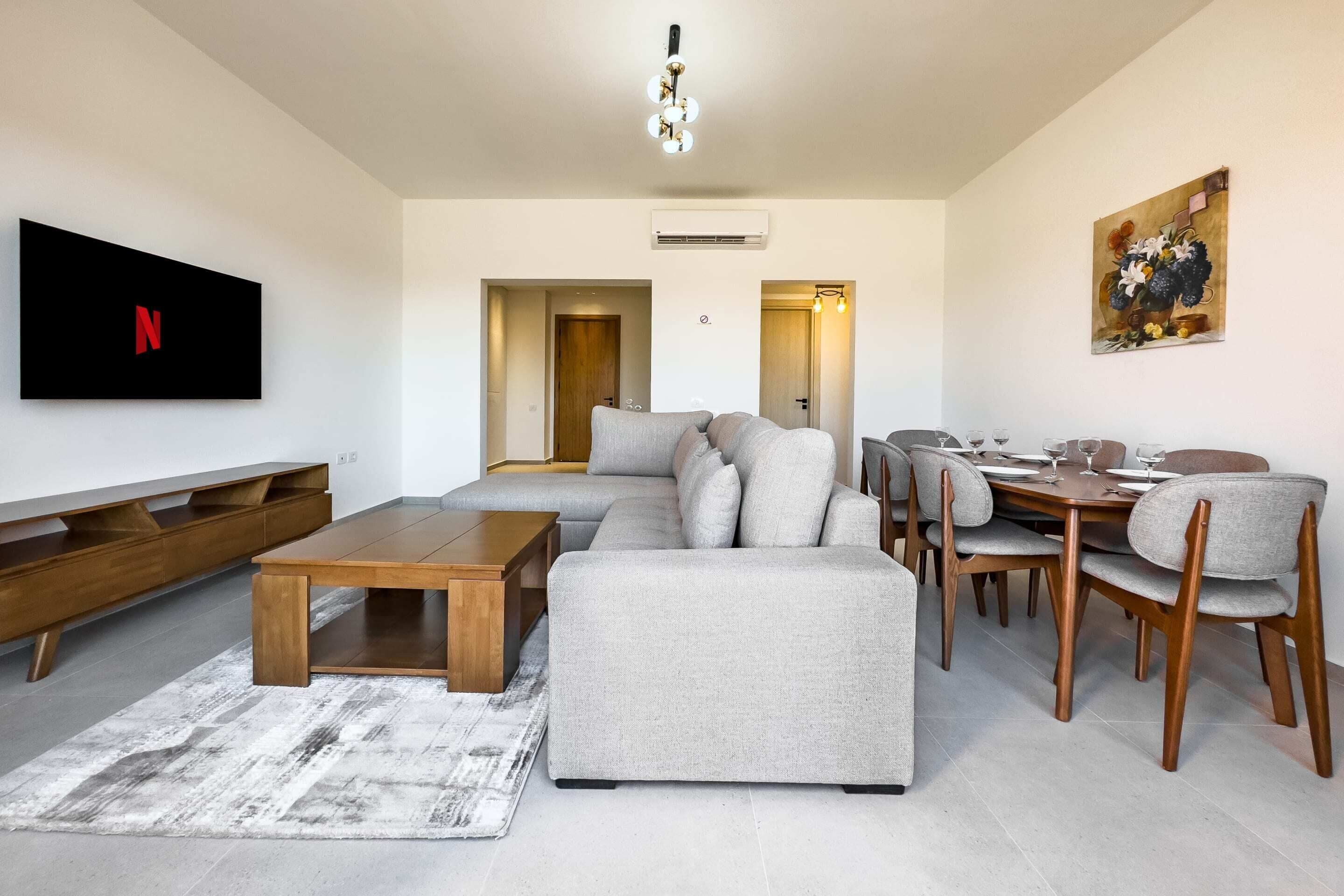 A modern living room with a sectional sofa, wooden coffee table, and dining area with chairs and a table.