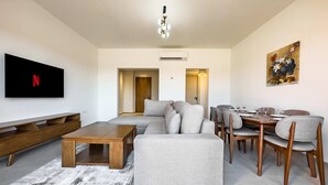 A modern living room with a sectional sofa, wooden coffee table, and dining area with chairs and a table. - Xuru Stays I Cool & Curated 1bdr @ Kamaran El Gouna (El Gouna)