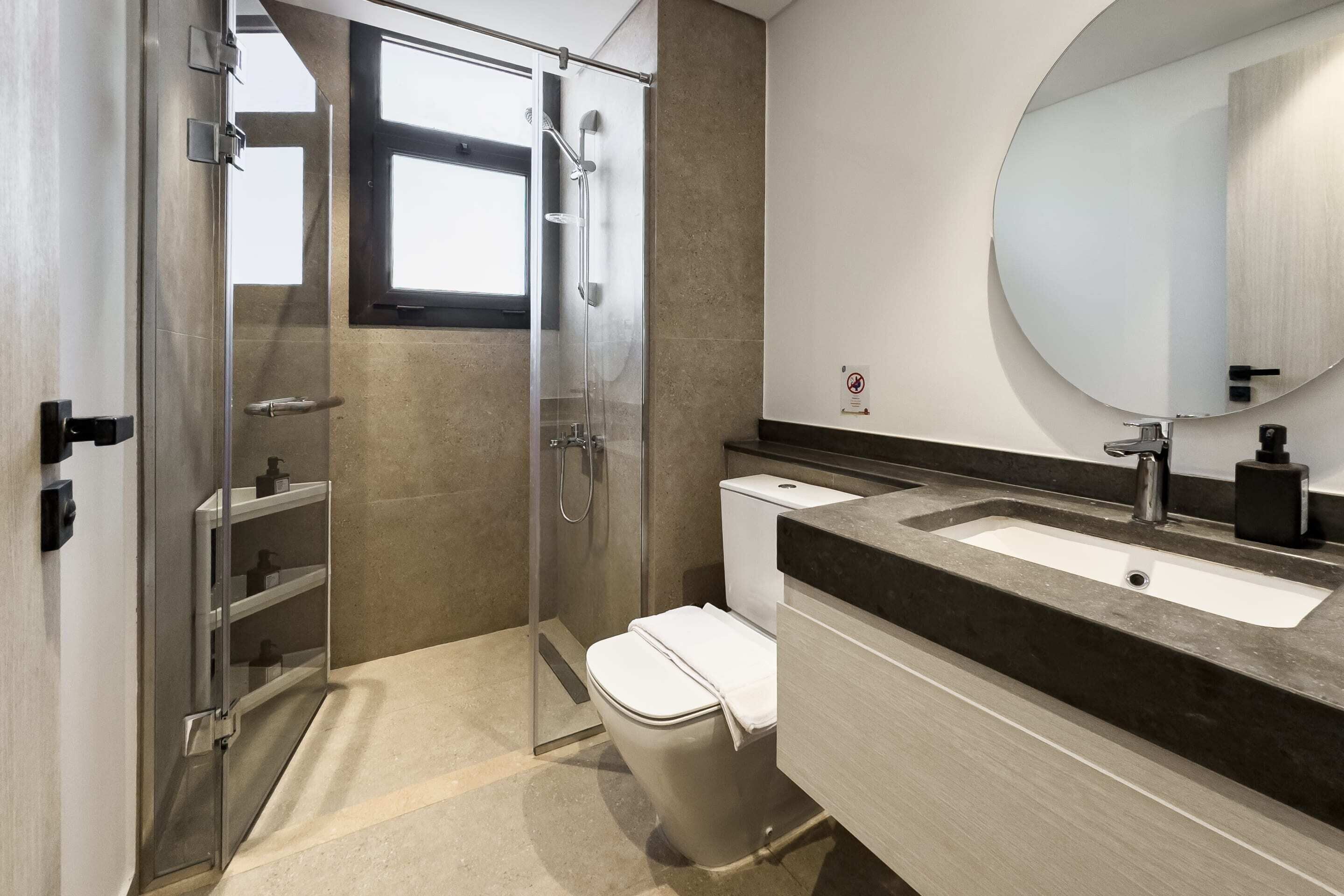 Ein modernes Badezimmer mit einer Duschkabine, einer weißen Toilette, einem Waschbecken mit dunkler Arbeitsplatte und einem großen Spiegel.