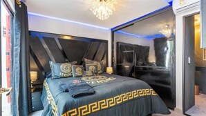 A modern bedroom with a large bed, a chandelier, and a sliding glass door to the outside.