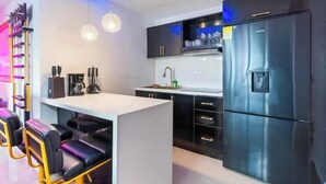A modern kitchen with black cabinets, a stainless steel refrigerator, and a bar area with stools.