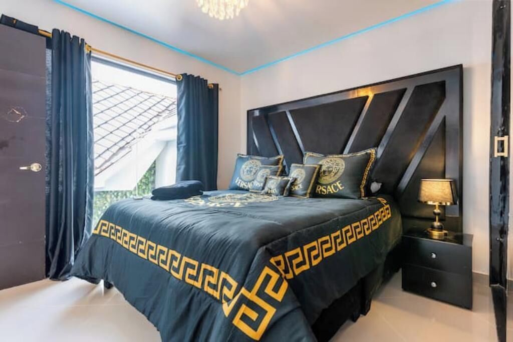 A bedroom with a bed, a nightstand, a lamp, and a view of the outdoors.
