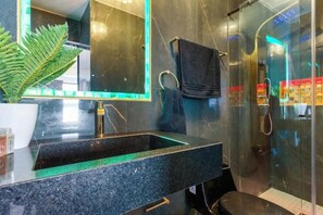 A modern bathroom with a granite sink, a large mirror, a towel rack, and a glass shower enclosure.