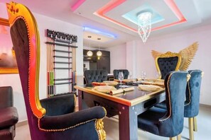 A dining area with a long table, black upholstered chairs with gold trim, and a chandelier.