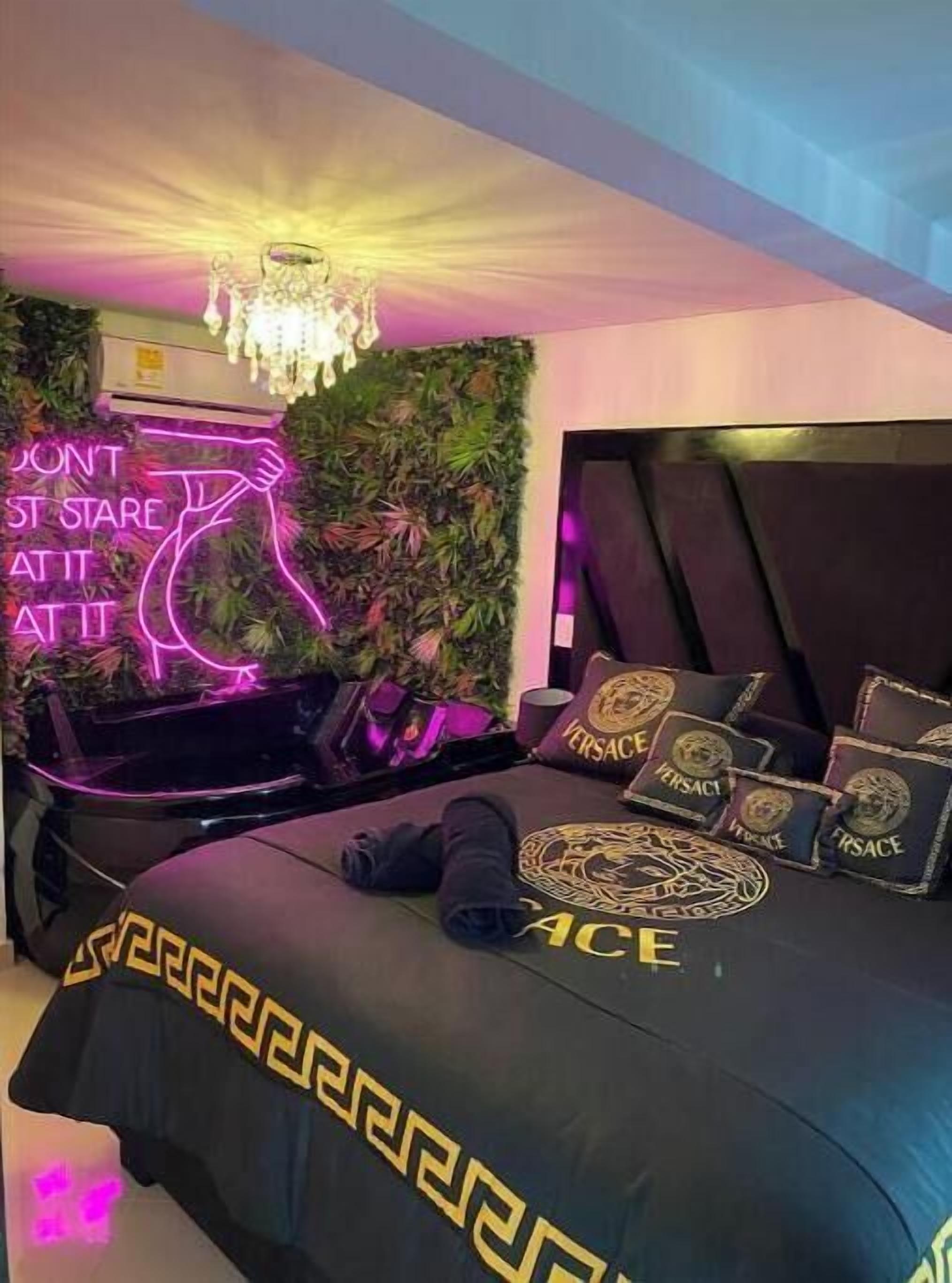 A modern bedroom with a black bed, neon sign, and a green wall.