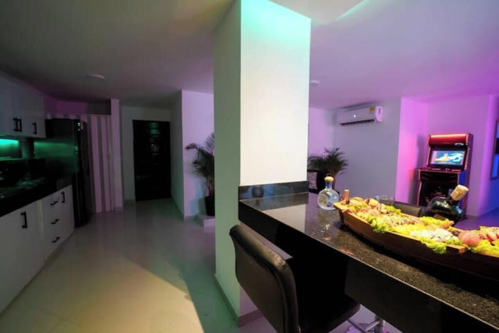 A modern kitchen with a long counter, a black chair, and a television on the wall.