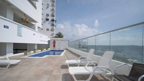 A rooftop pool area with lounge chairs, a small pool, and a glass railing overlooking the sea. - Serenity Escape (CARTAGENA BOLIVAR)