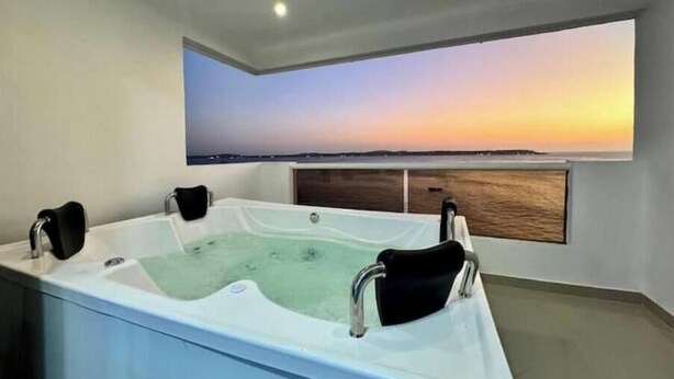 A modern bathroom with a large bathtub and a view of the sunset over the ocean. - Serenity Escape (CARTAGENA BOLIVAR)