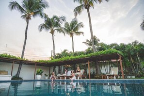 A poolside area with lounge chairs and a covered seating area, surrounded by palm trees. - Vila Aytana Carlore (Paracuru)