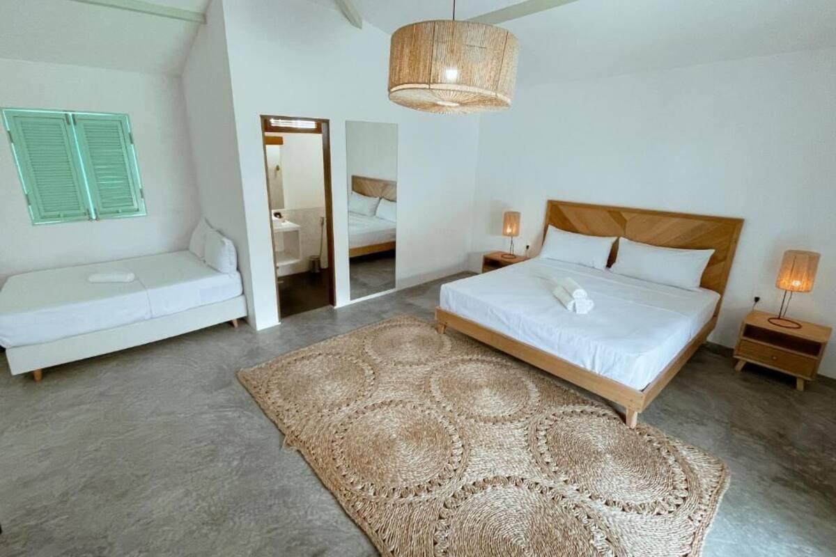 A bedroom with a bed, bedside tables, a hanging light fixture, a woven rug, and a mirror.