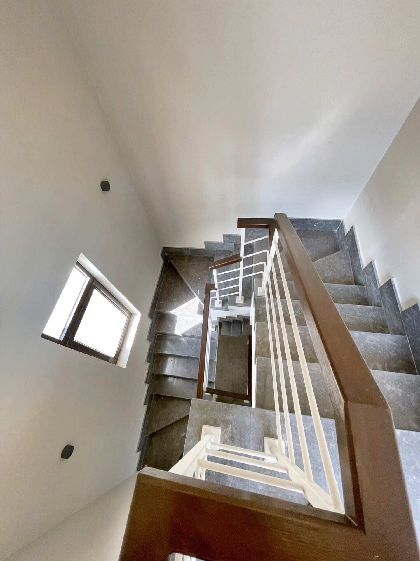 Una escalera moderna con barandilla de madera y un ventanal pequeño a la izquierda.