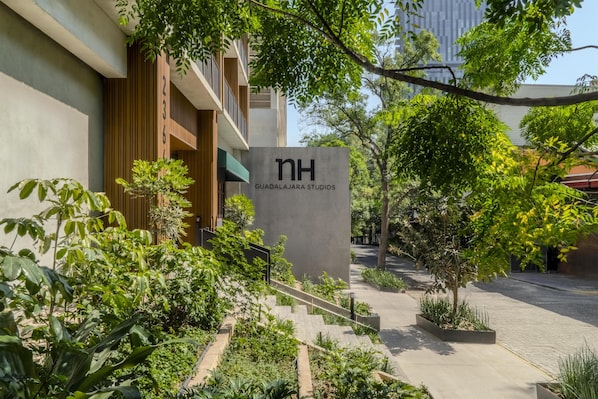 Un edificio con un letrero que dice 'nh GUADALAJARA STUDIOS' y una escalera rodeada de vegetación.