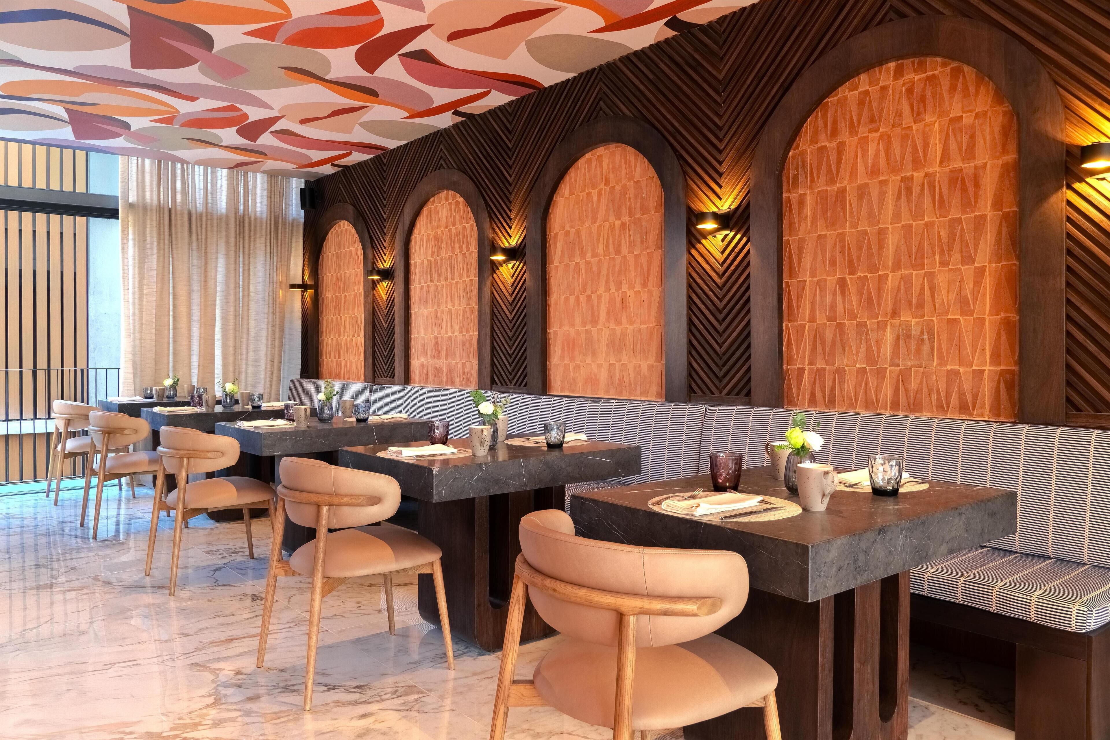 A modern restaurant with marble flooring, wooden chairs, and a long counter with tables.