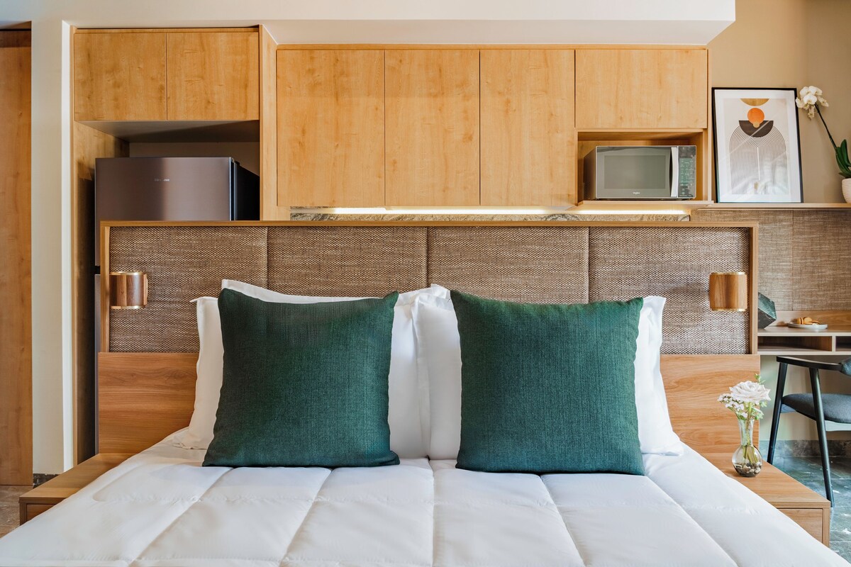 Una camera d'albergo con un letto, angolo cottura, televisione e un piccolo tavolo con un vaso.