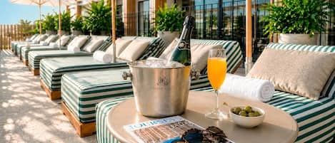 Un espace aménagé au bord de la piscine, avec des chaises longues, un seau à champagne, un verre de jus d’orange et un bol d’olives.